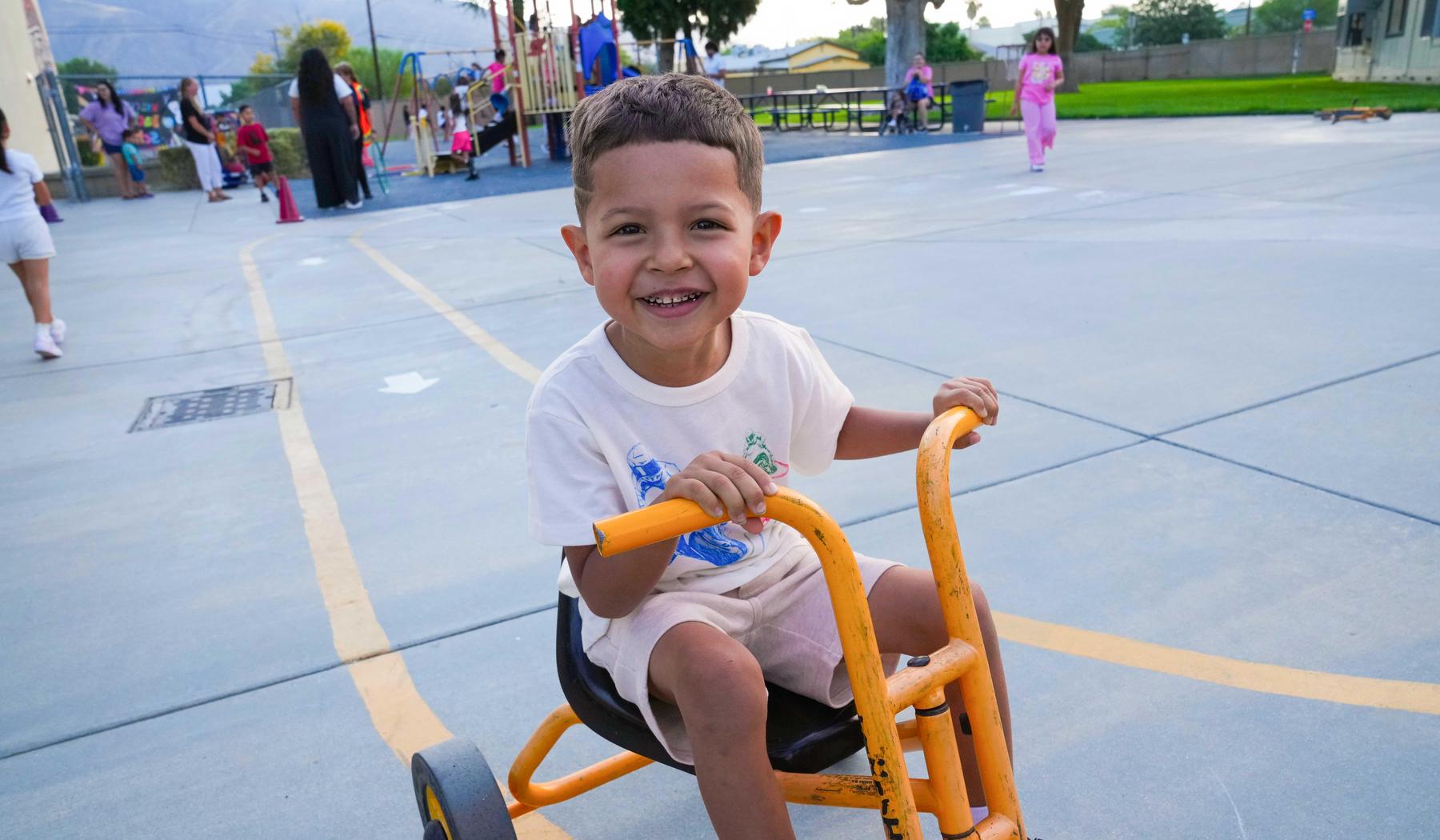 young boy riding a yellow trike at school