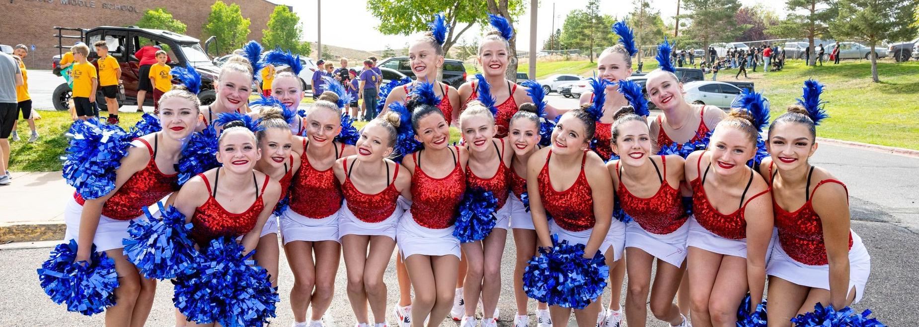 Cheerleaders in red and white outfits posing together with blue pom-poms.