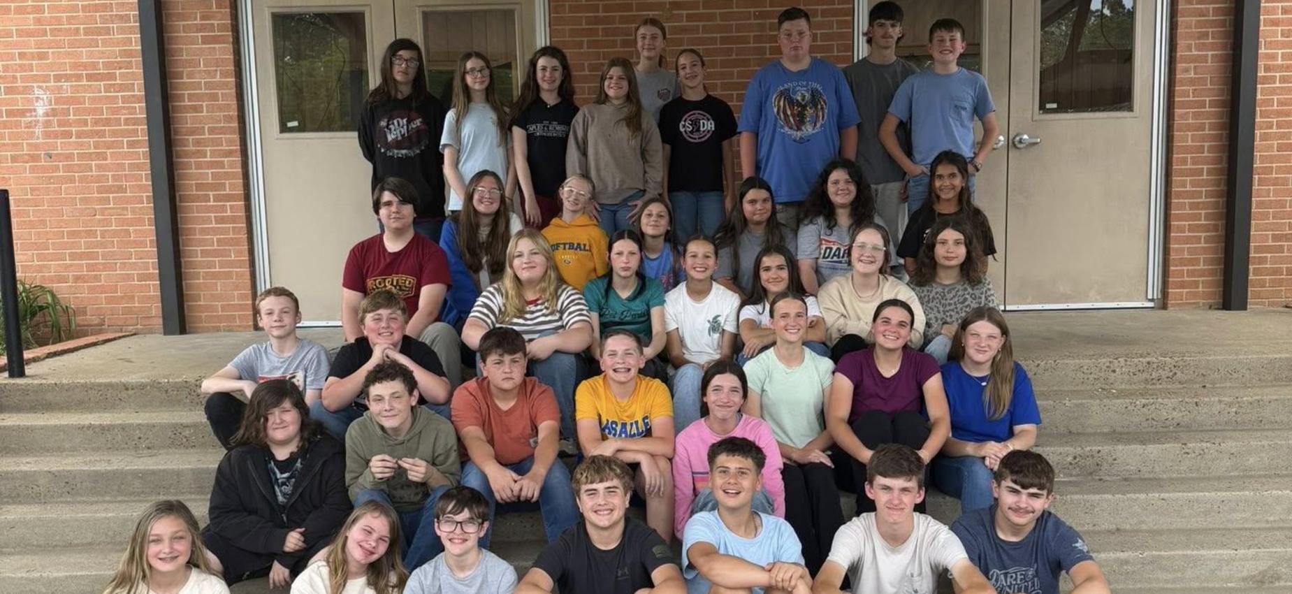 Large group of students sitting on steps, smiling and posing for a group photo.