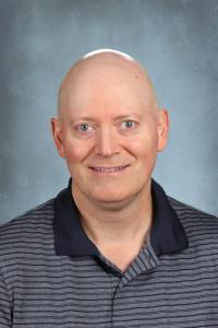 Bald man wearing a striped polo shirt against a gray background.