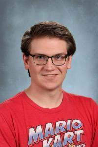 Man with glasses and a red t-shirt featuring Mario Kart, smiling against a blue background.