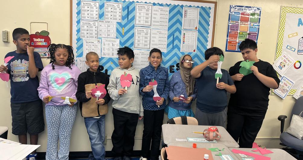 Students holding colorful paper cutouts in a classroom setting.