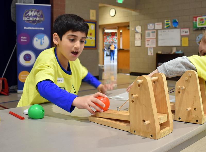 A child plays with a catapult and colorful balls in a classroom setting.