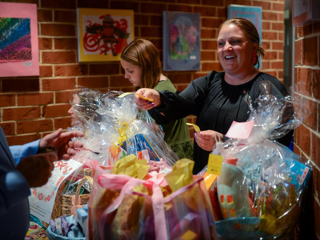 Two parents selling raffle tickets in front of a table full of baskets.