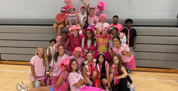 Group of people dressed in pink clothing, celebrating together in a gym.