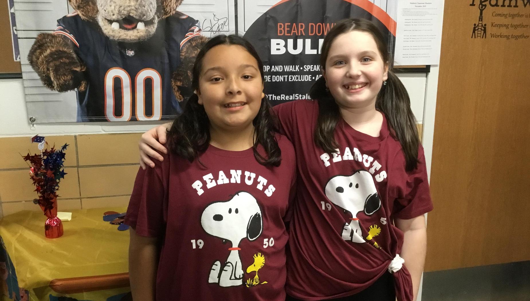 Two girls in matching maroon Peanuts t-shirts smiling together.