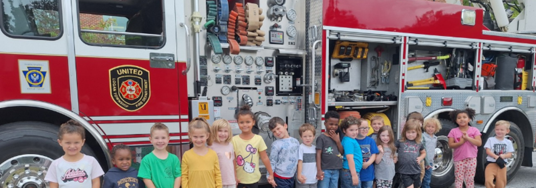 A group of children smiling in front of a fire truck with various equipment visible.