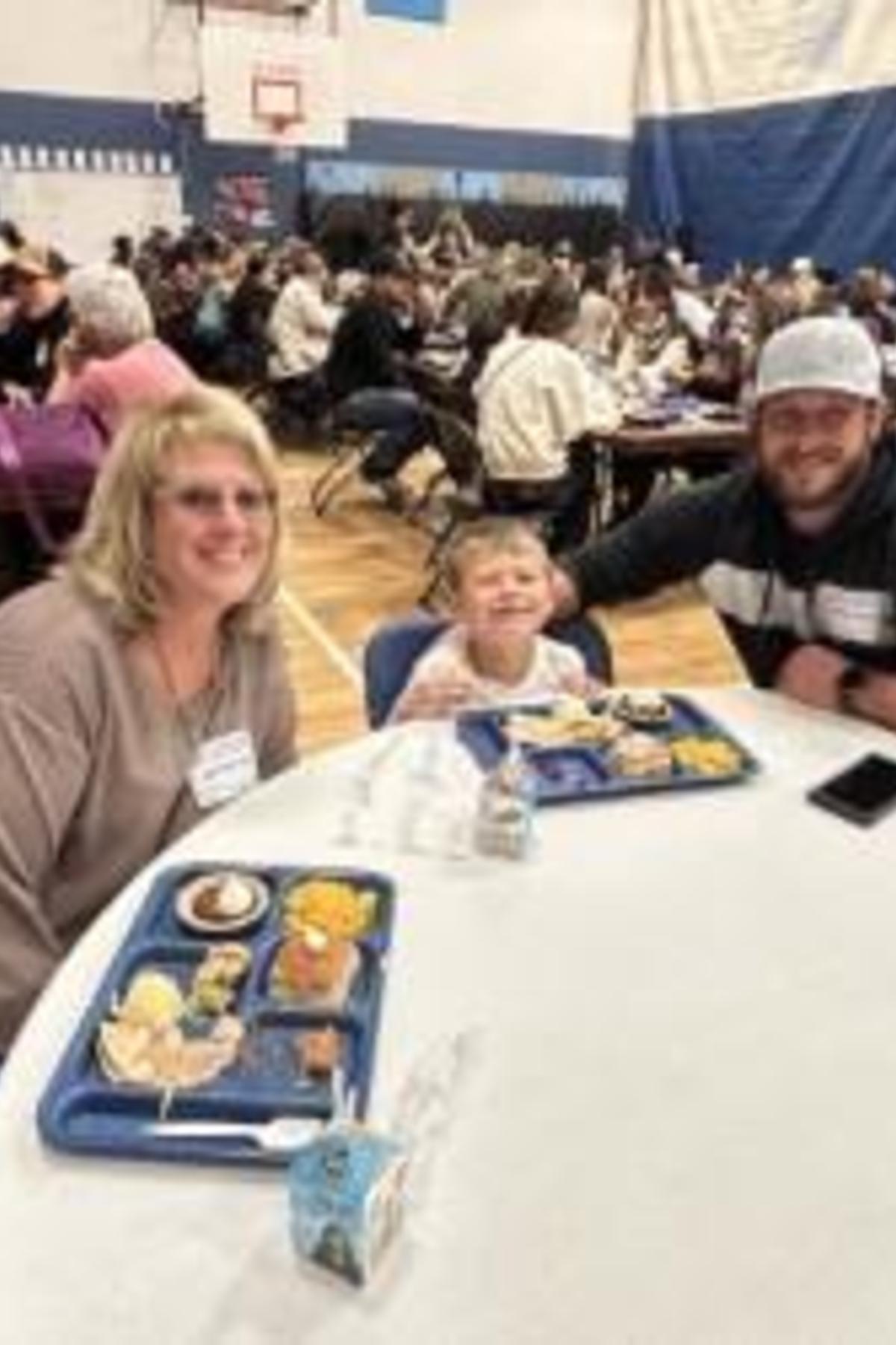 A family enjoying a meal together at a gathering, with food trays and smiles.