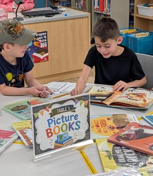 Two boys reading together at a table with a sign for picture books.