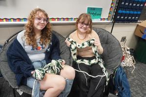 Two students hold up a long string they have crocheted to maybe be a blanket or scarf.