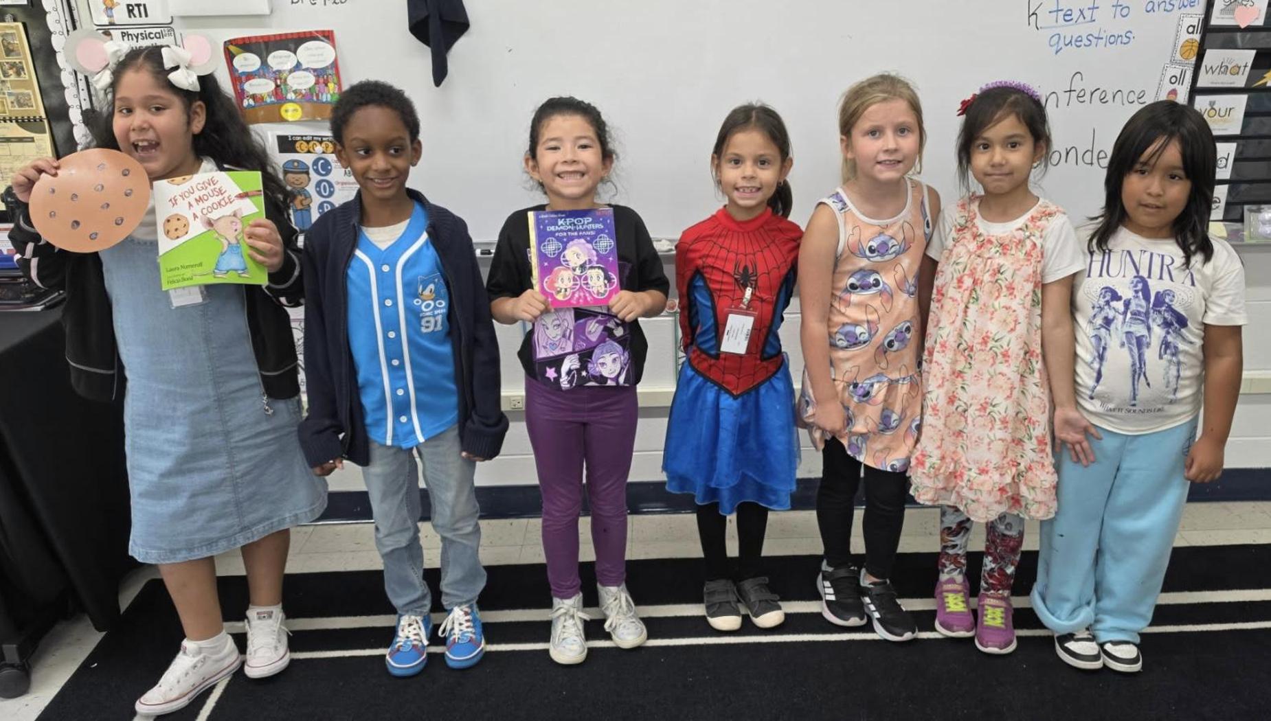 A group of children in costumes proudly display their books.