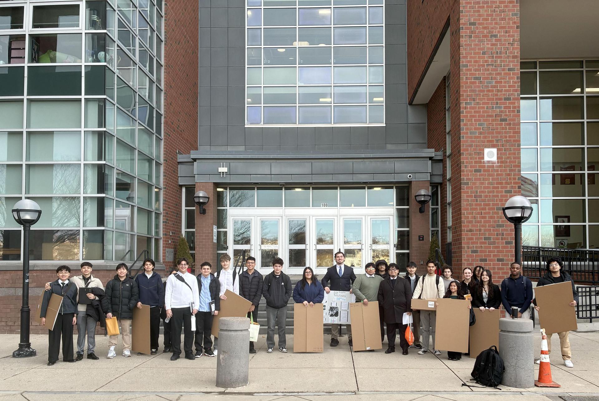Group of students holding cardboard signs outside a school entrance.