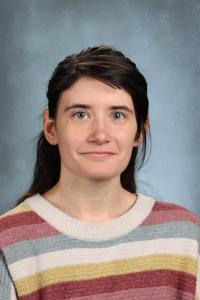 Young woman with long hair in a colorful sweater, staring directly at the camera.