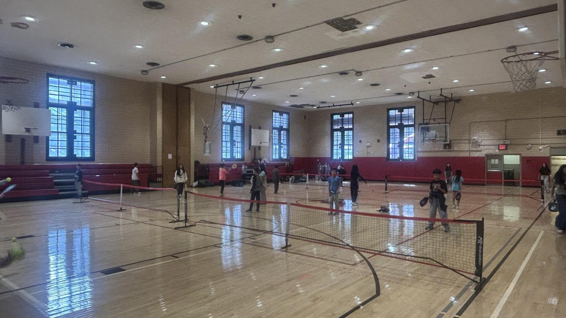 A gymnasium with people playing tennis and badminton on multiple courts.