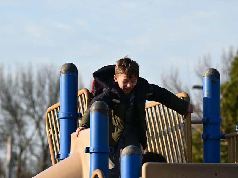 A boy joyfully climbs on a playground structure with clear blue skies in the background.