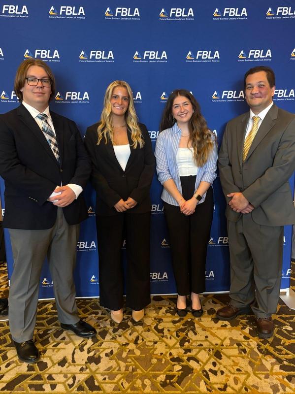 three students and one teacher in suits in front of FBLA signage