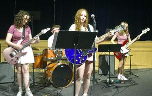 Four young musicians perform together, featuring guitars and drums on stage.