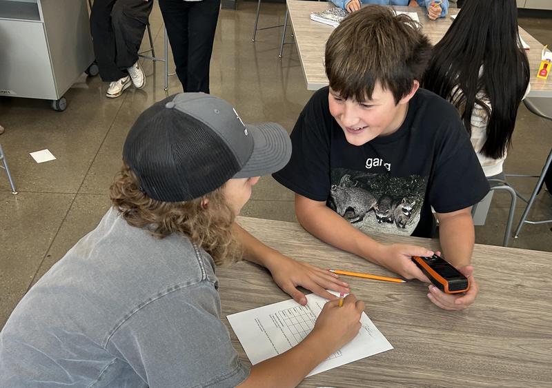 A student with a handheld air-quality sensor and a student with a worksheet prepare to conduct air-quality experiments.