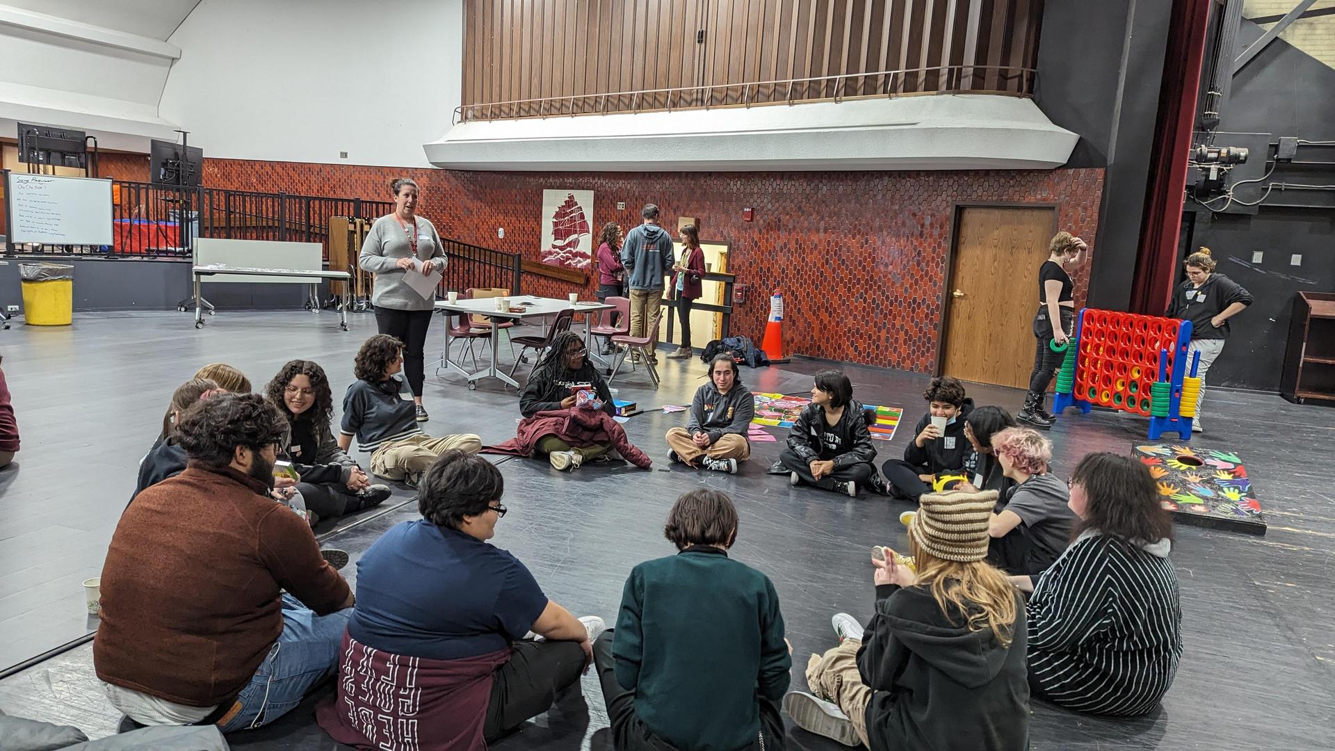 A circle of teenagers sitting on the ground with an adult reading from a paper