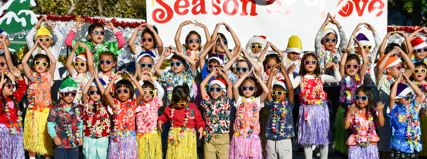 Children wearing Hawaiian shirts and sunglasses celebrate in front of a holiday backdrop.
