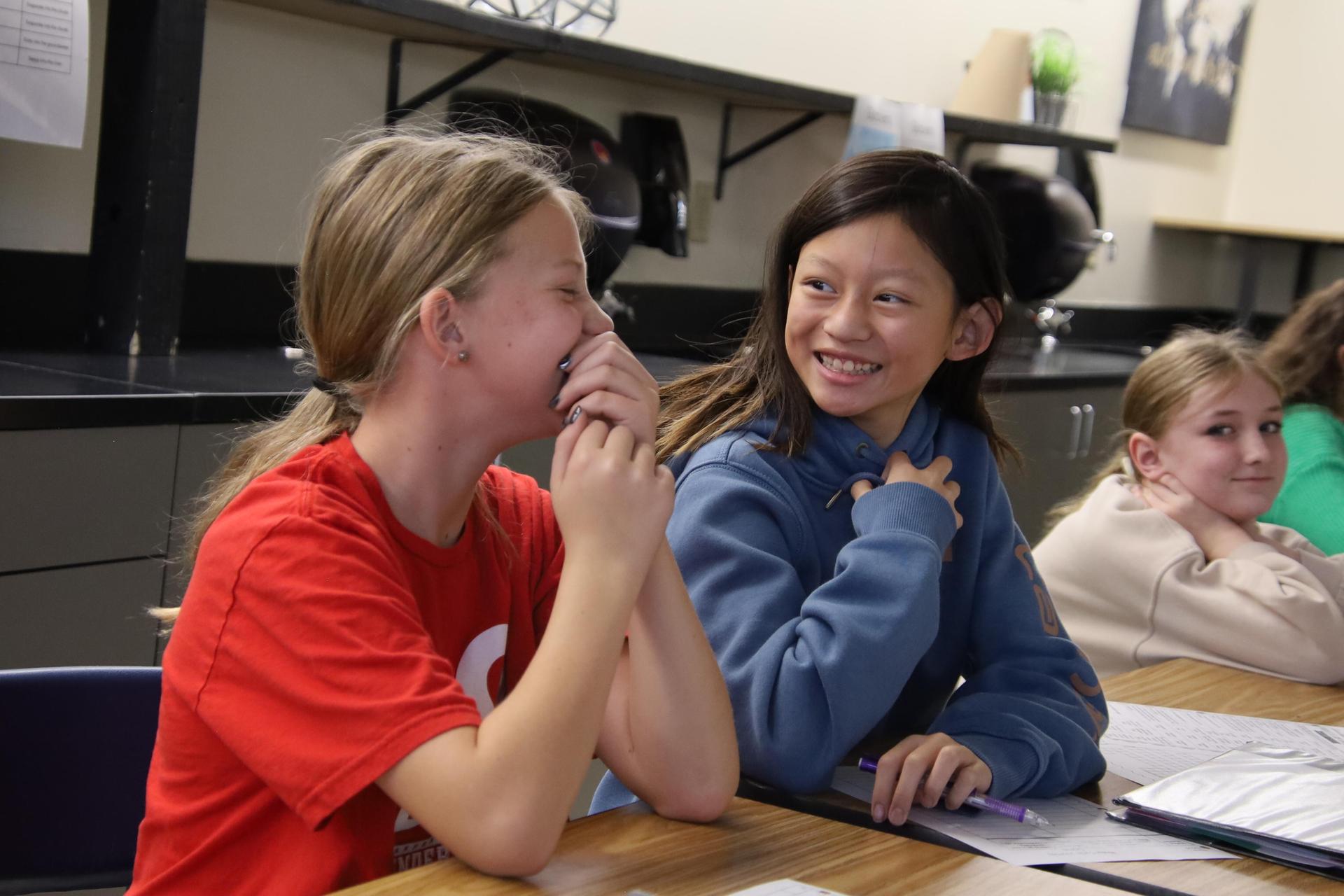 two middle school girls laughing and smiling in a science classroom