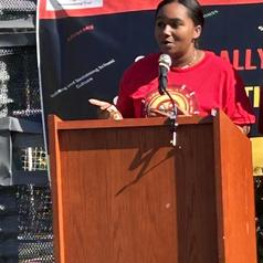 Person speaking at a podium during an outdoor event.