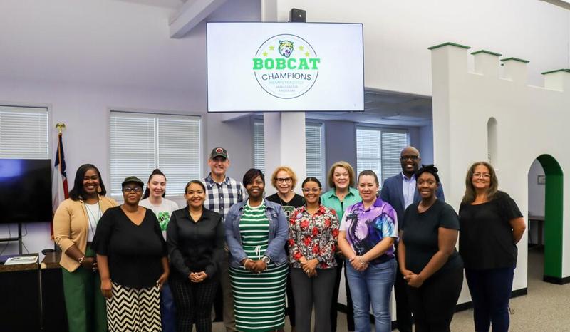 Group of people standing in front of a screen displaying 'Bobcat Champions' logo.