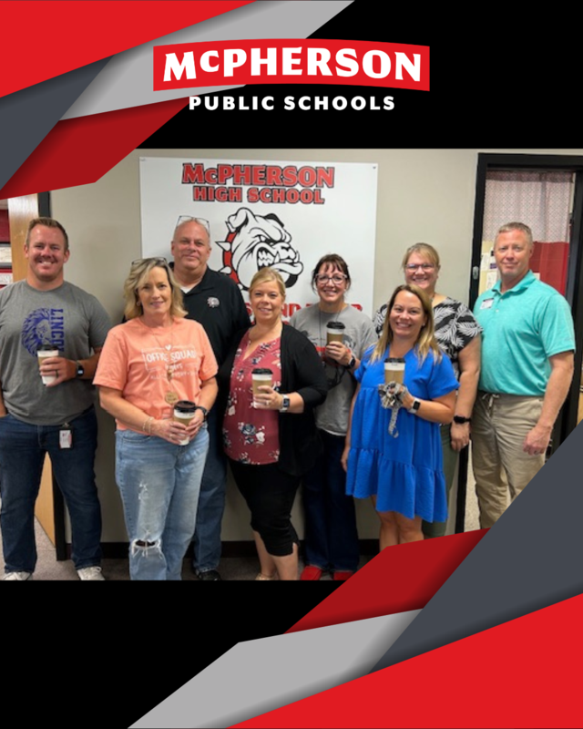 A group of 8 adults holding coffee cups in front of a McPherson High School Bullpups sign