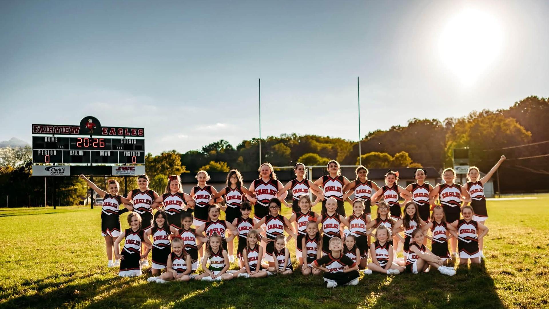 Cheerleading squad posing together on a football field near a scoreboard.