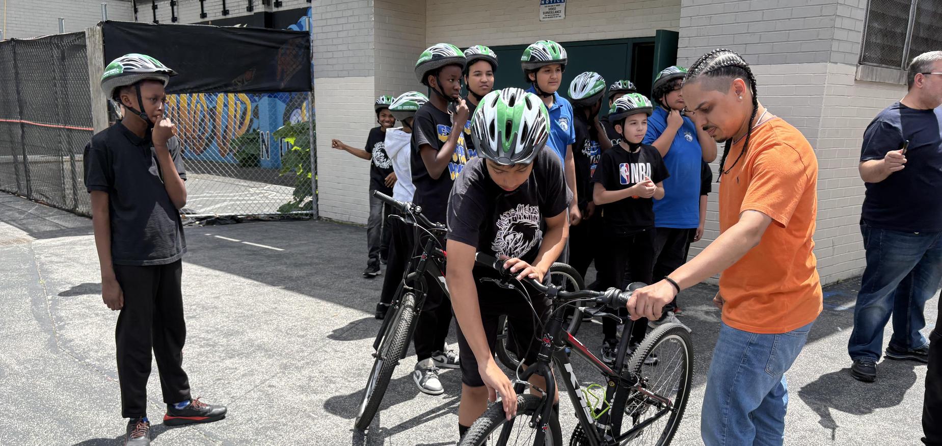 Staff showing student how to get on a bicycle with other students in the background watching them