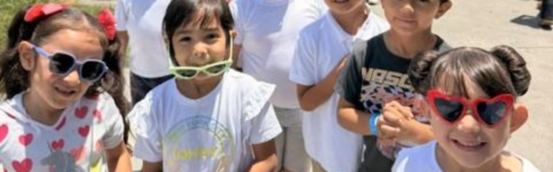 A group of children wearing sunglasses and smiling for a photo outdoors.