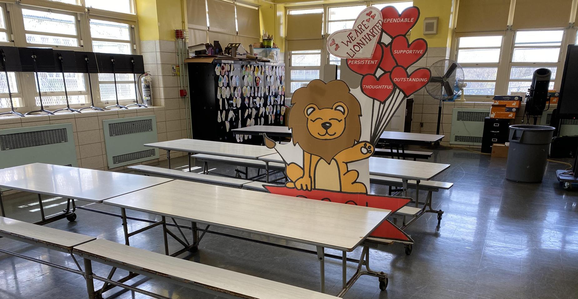 Cafeteria with tables and a lion mascot holding balloons in the center.