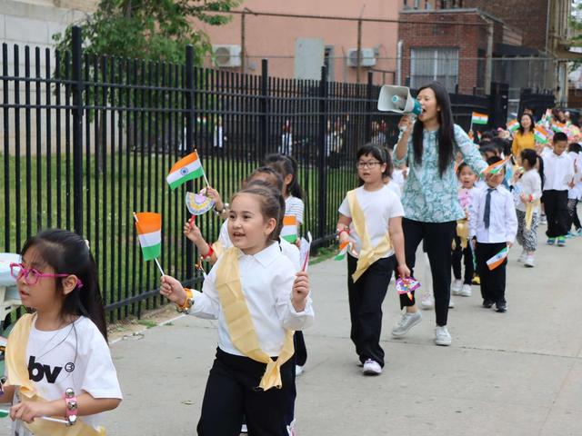 Children in a parade holding flags and celebrating with a leader using a megaphone.