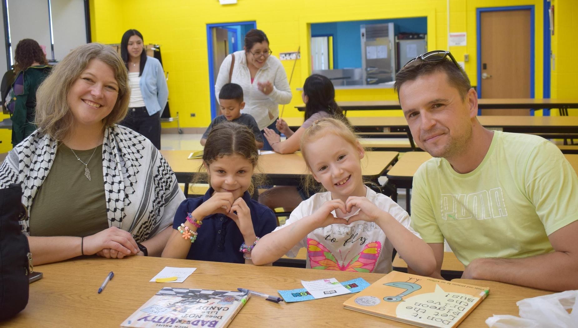 Family of four smiling at a table in a colorful school cafeteria.