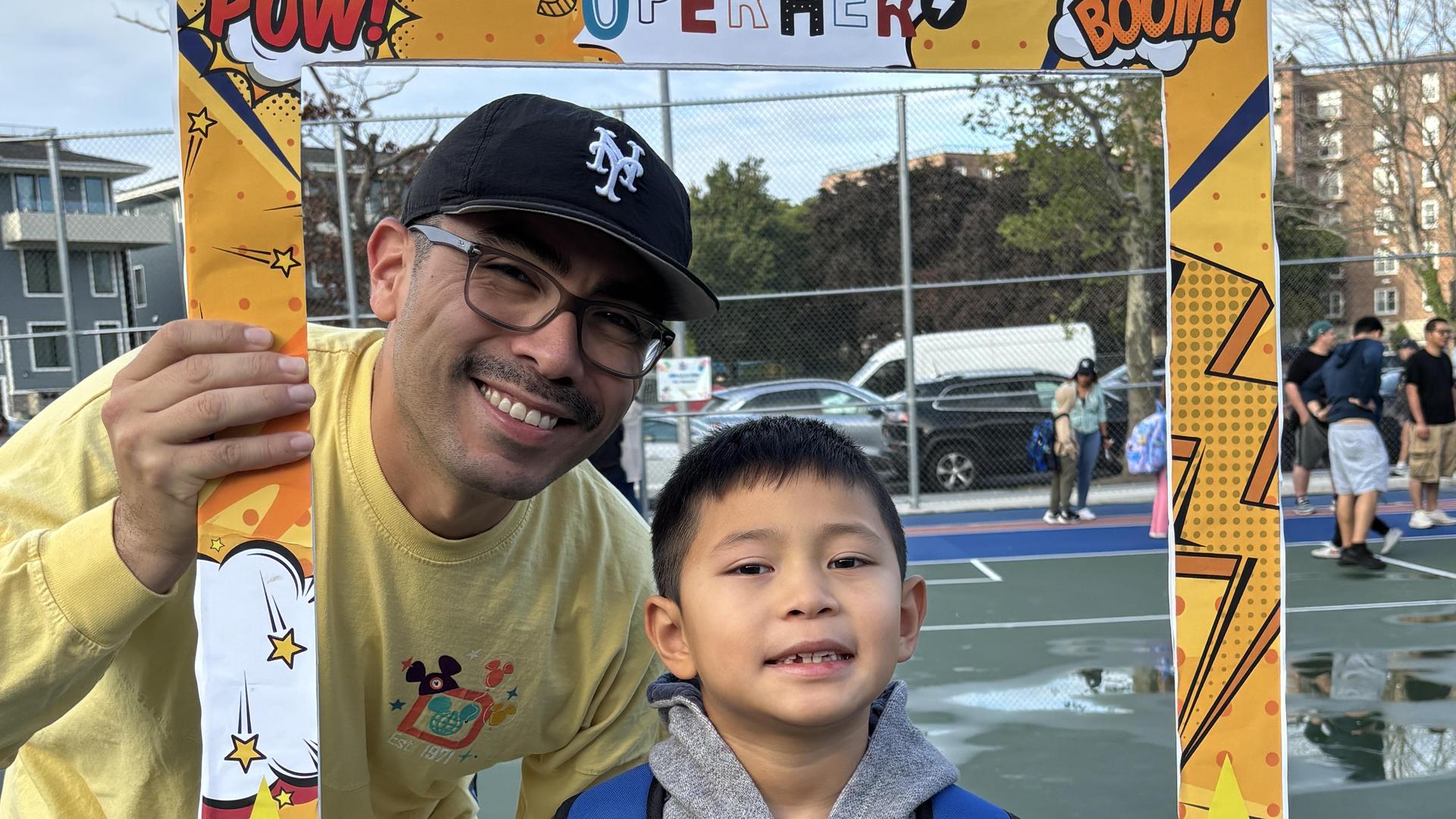 A man and young boy posing happily with a colorful frame, wearing backpacks.