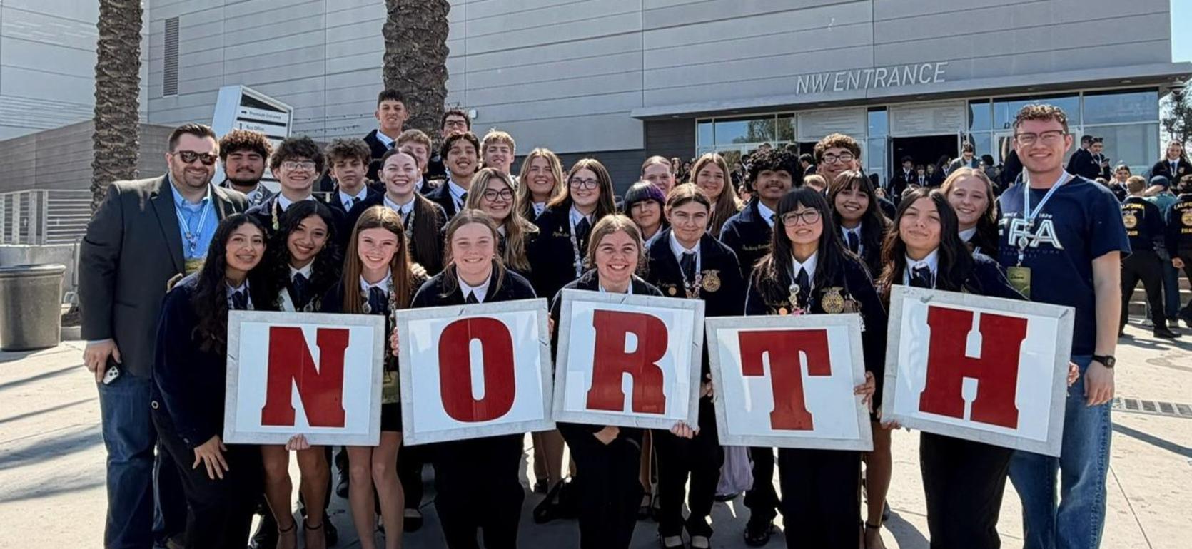 A group of students holding a large sign that says 'NORTH' outside a building.