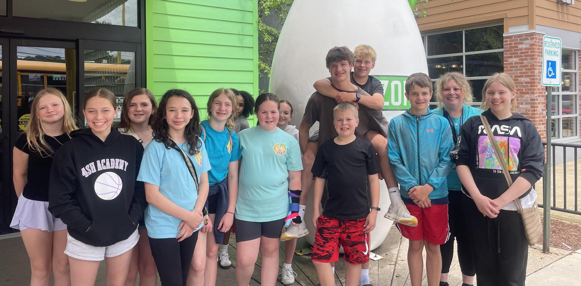 Group of young teens poses outside a colorful building with a giant statue.