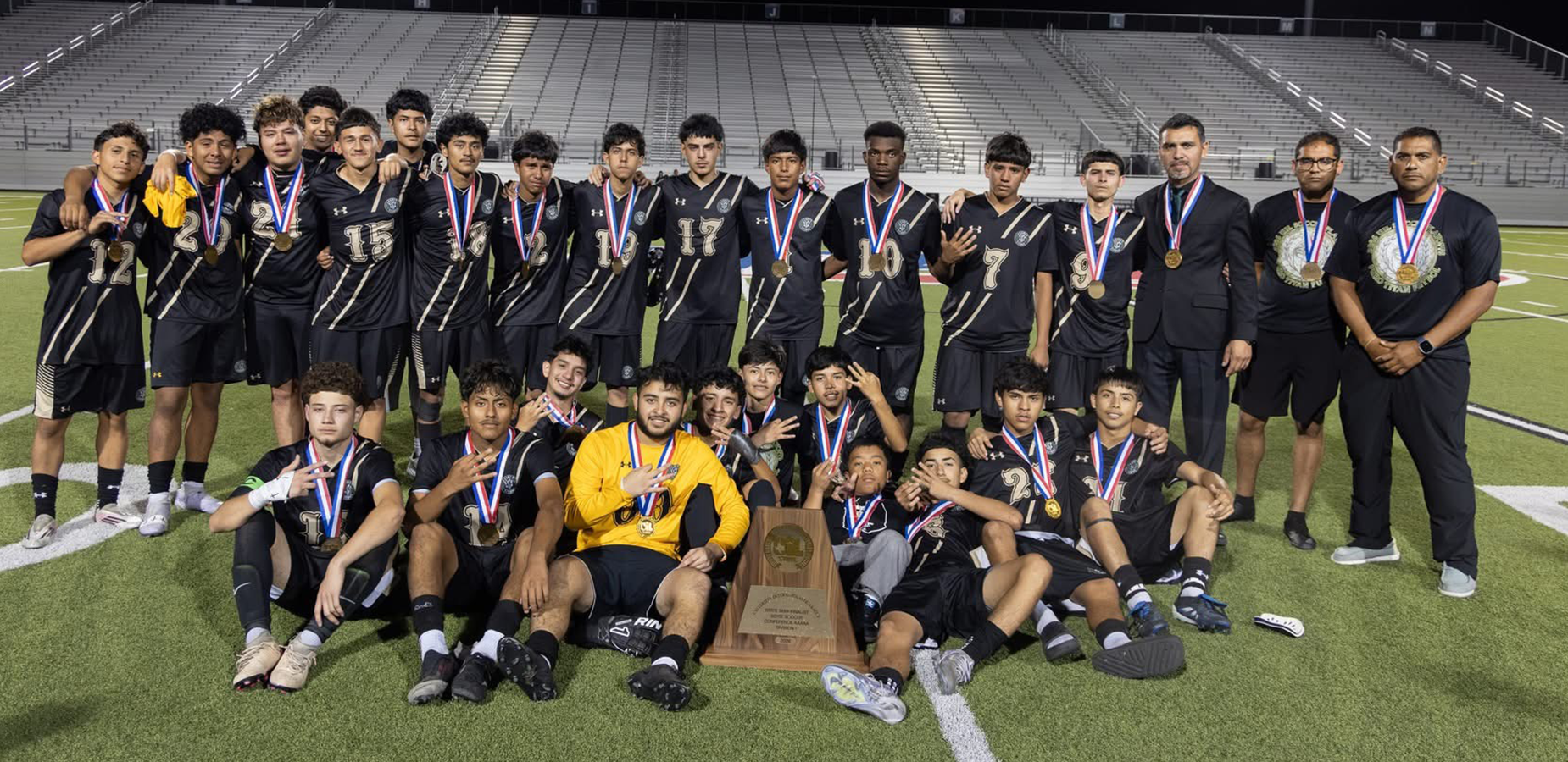 A soccer team poses together with medals and a trophy after a successful match.