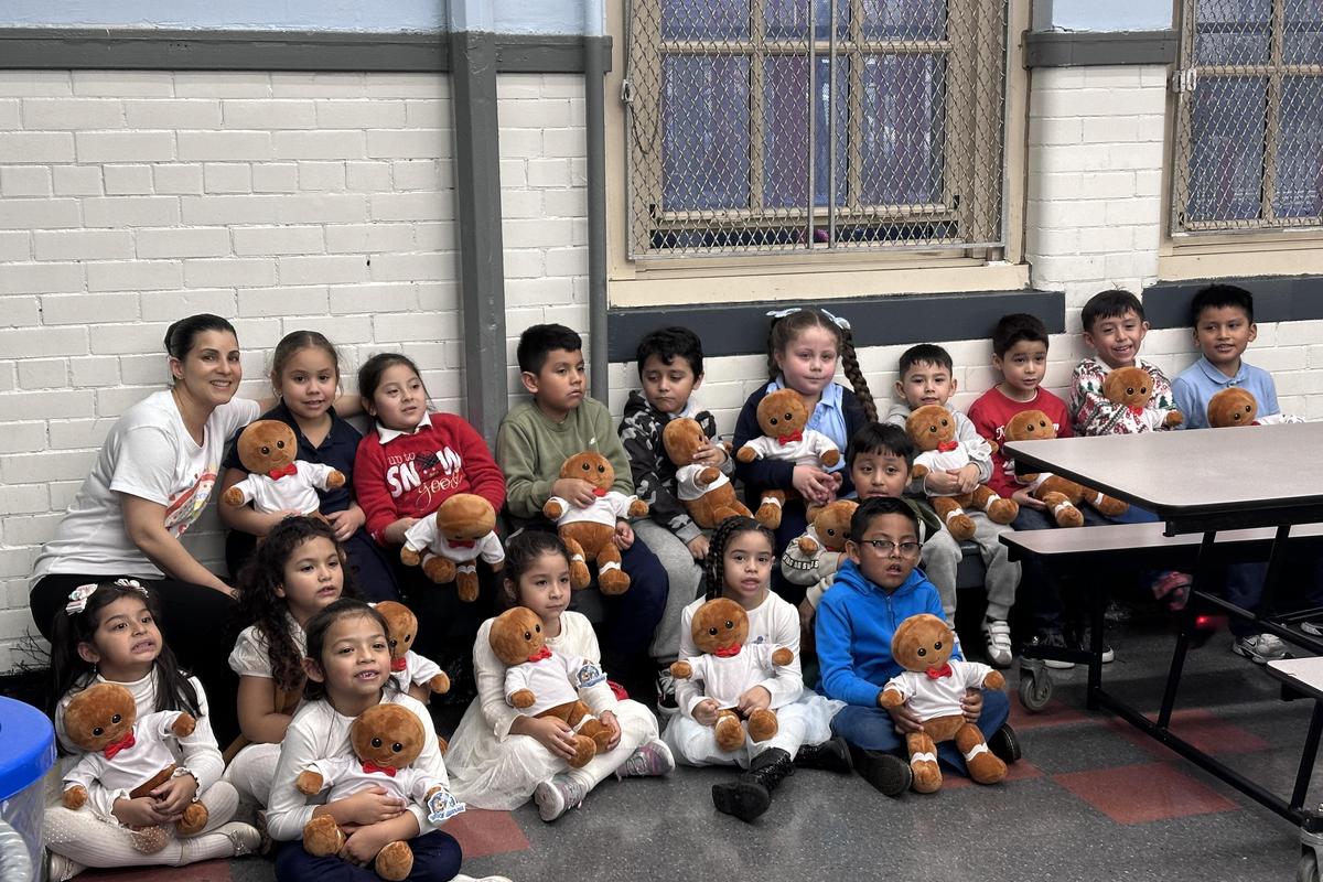 Group of children holding teddy bears with a teacher in a classroom setting.