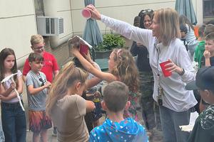 Harrison Park Elementary teacher, Mrs. Kelly Pratt, tests out a student's umbrella by dumping water over her head