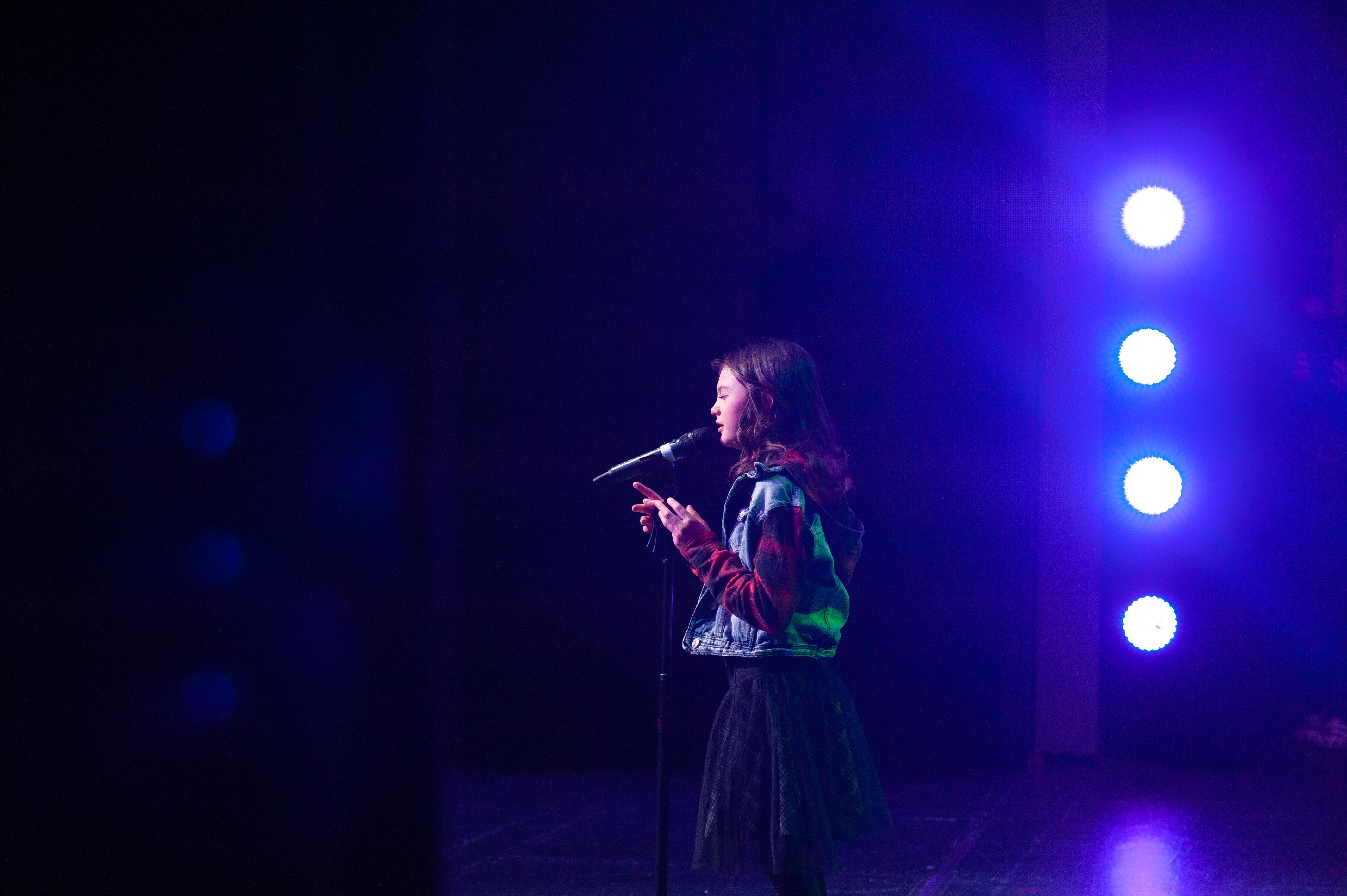 Female singer stands alone on stage illuminated by stage lights