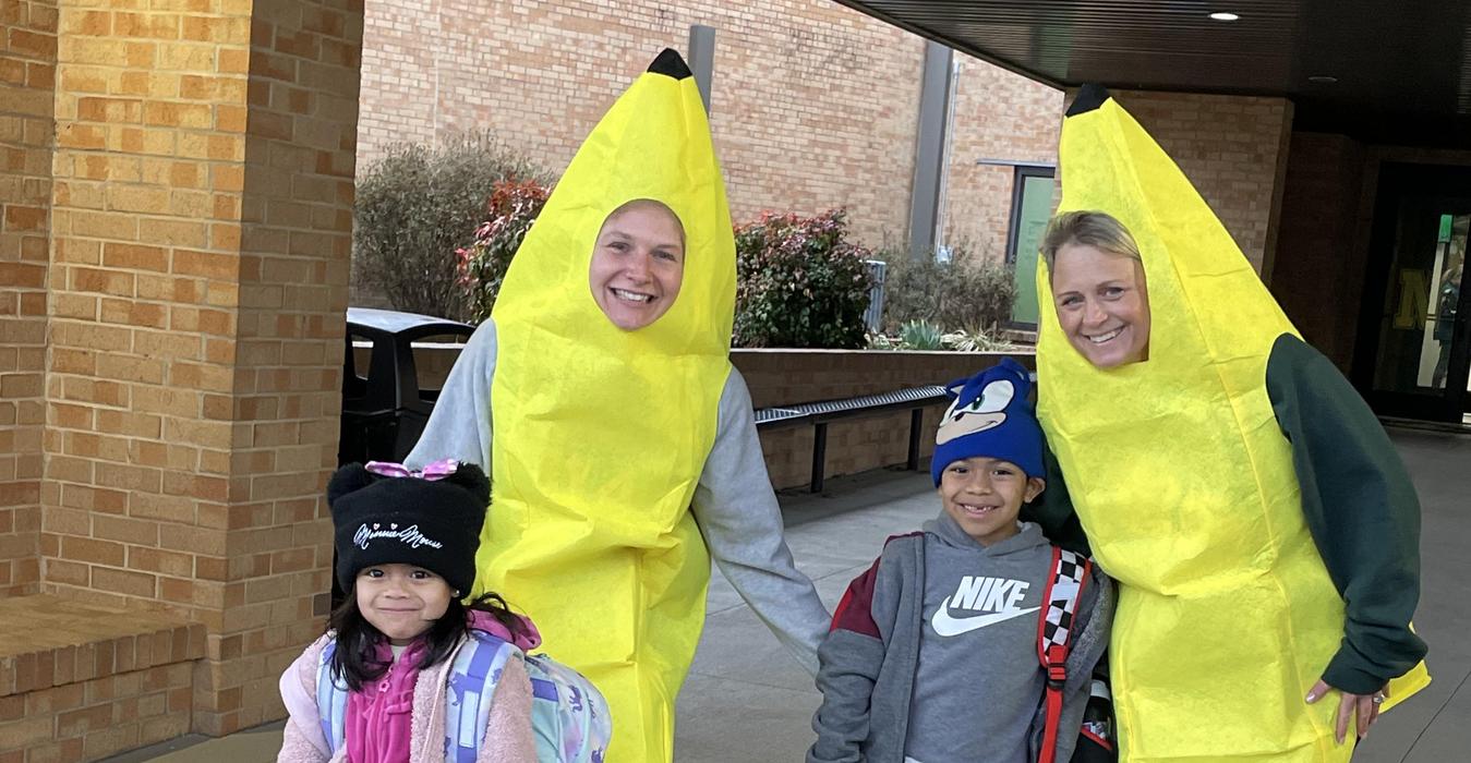 Two adults and two children dressed in banana costumes, smiling outdoors.