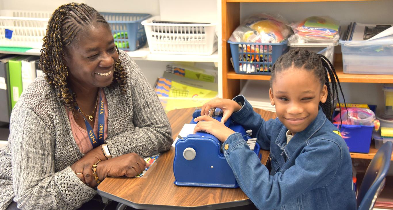 a student and teacher smile with braille writers