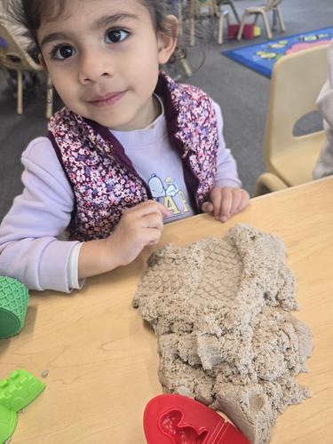 Child playing with sand on a table in a colorful classroom.