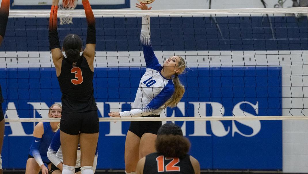 A volleyball player attempts to spike the ball over the net against an opposing player.