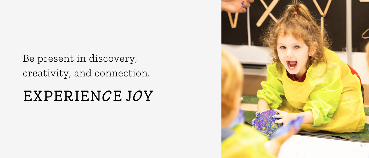Young girl in a yellow smock joyfully playing with colorful materials in an educational setting.
