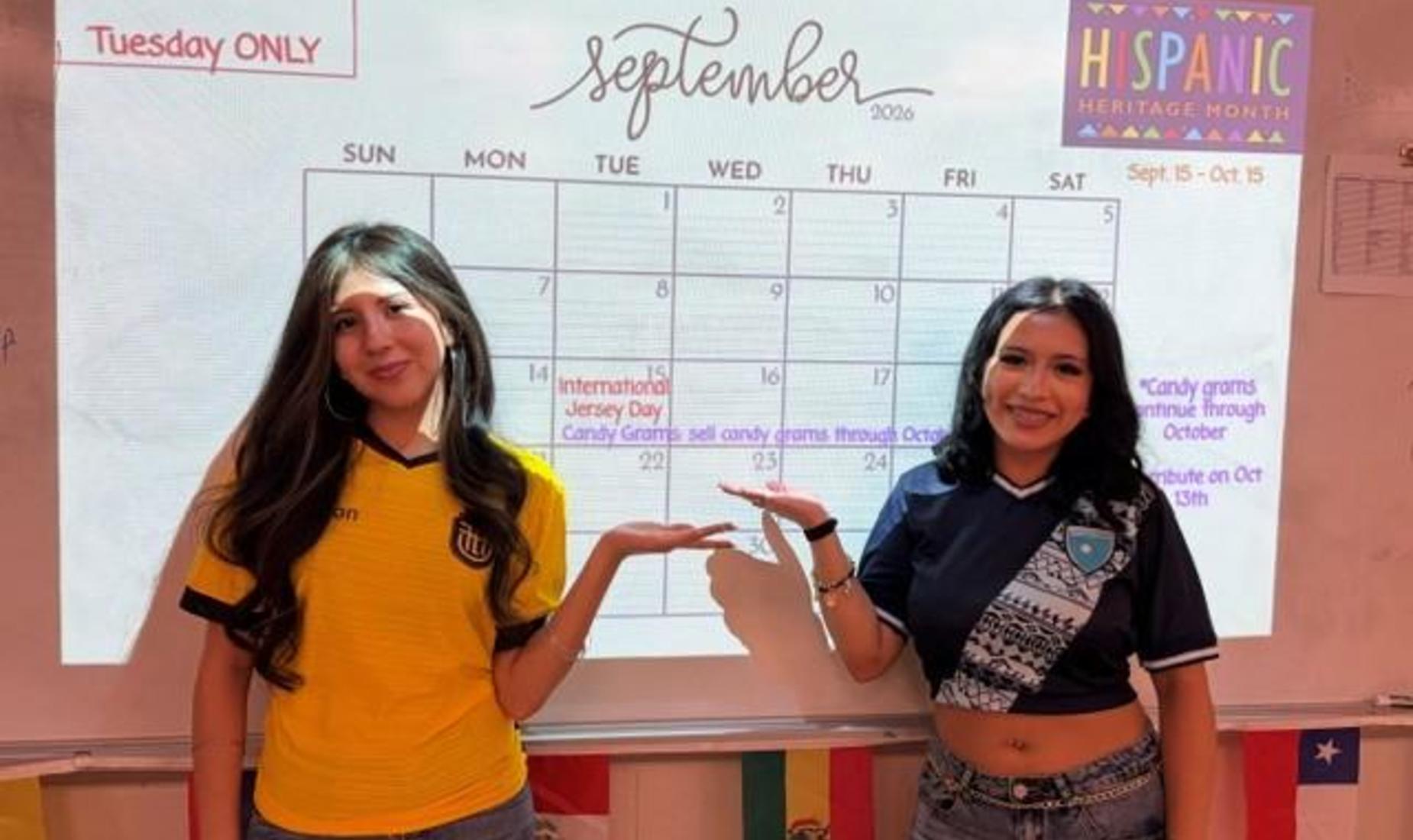 Two women stand in front of a calendar for September 2026, celebrating Hispanic Heritage Month.