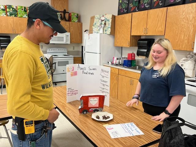 A student presenting a food truck idea to another person in a classroom setting.