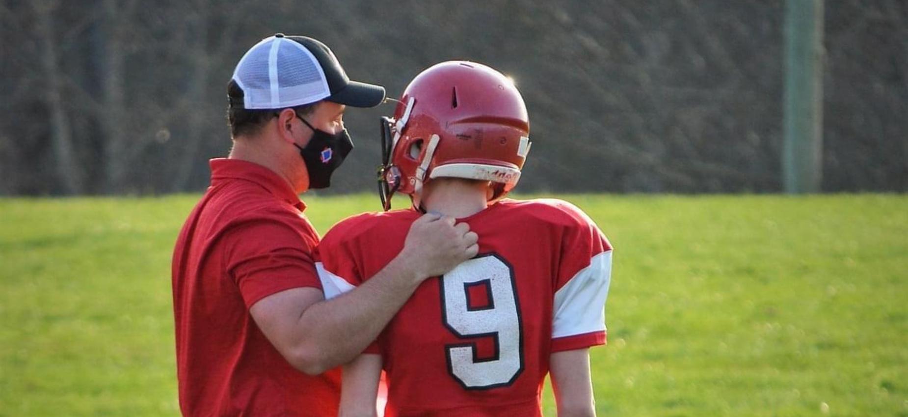 A football coach talks to a player on the sidelines.