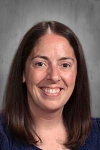 Smiling woman with long dark hair in a floral top against a gray background.